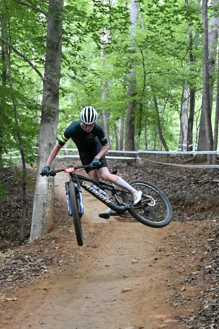 Rider launching off a lip on a wooded singletrack